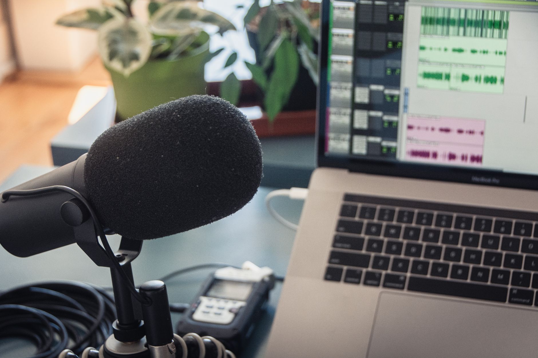 Person recording a podcast into a microphone with a laptop nearby